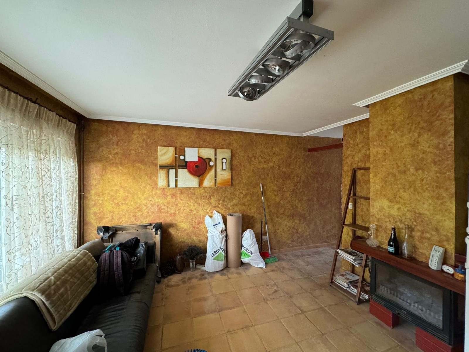 Salón antes de la obra: paredes de estuco dorado, suelo de baldosa de barro y chimenea