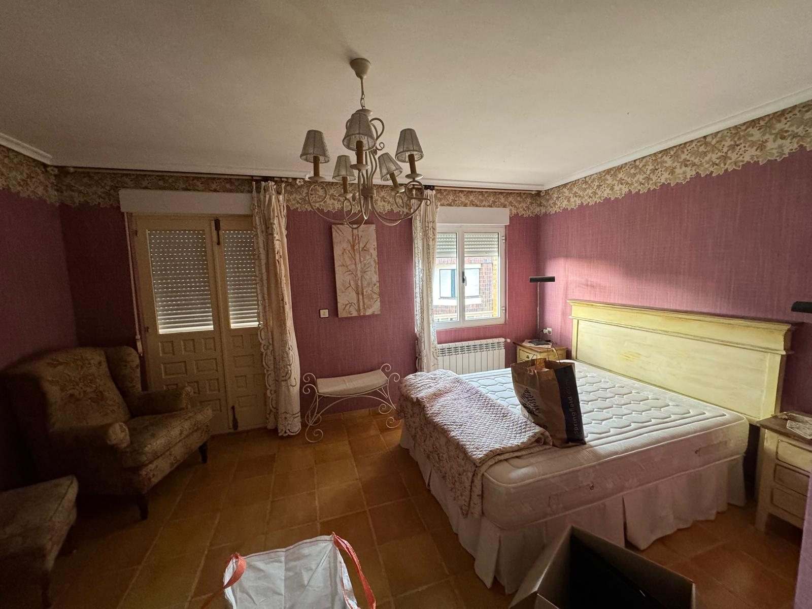Dormitorio con papel pintado granate, cenefa y lámpara de brazos