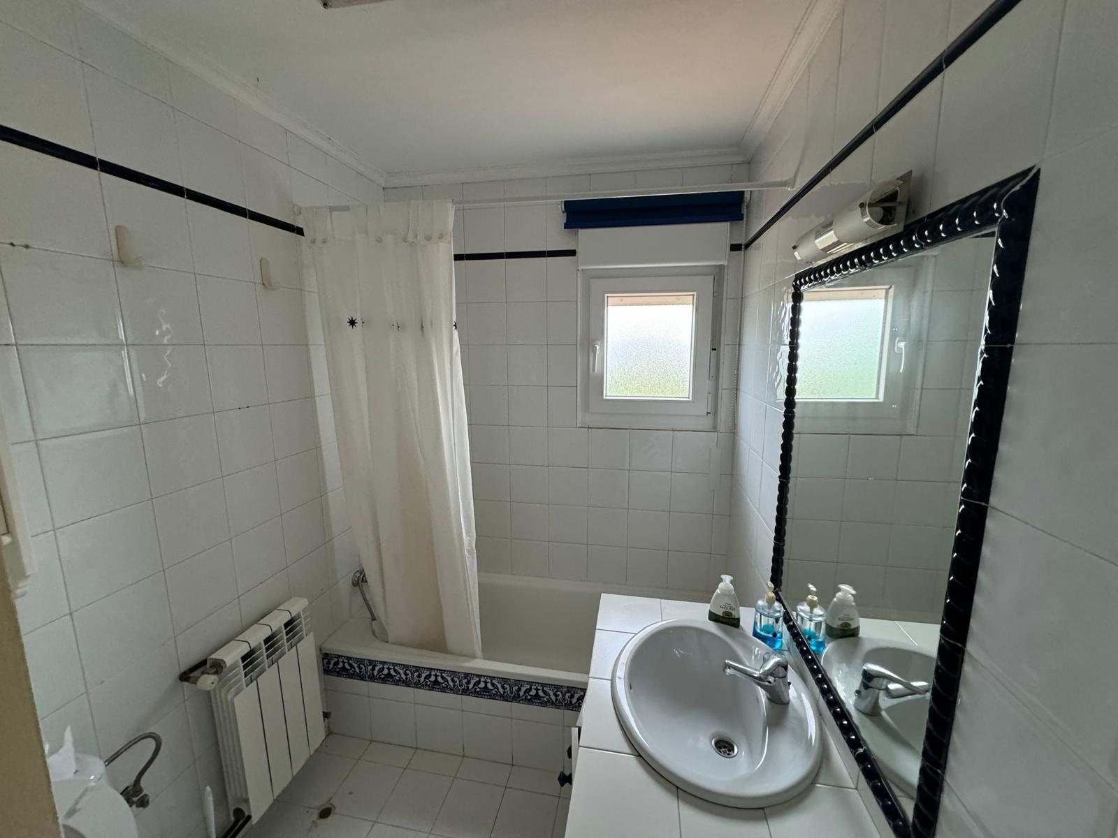 Baño alicatado en blanco con bañera, lavabo y espejo