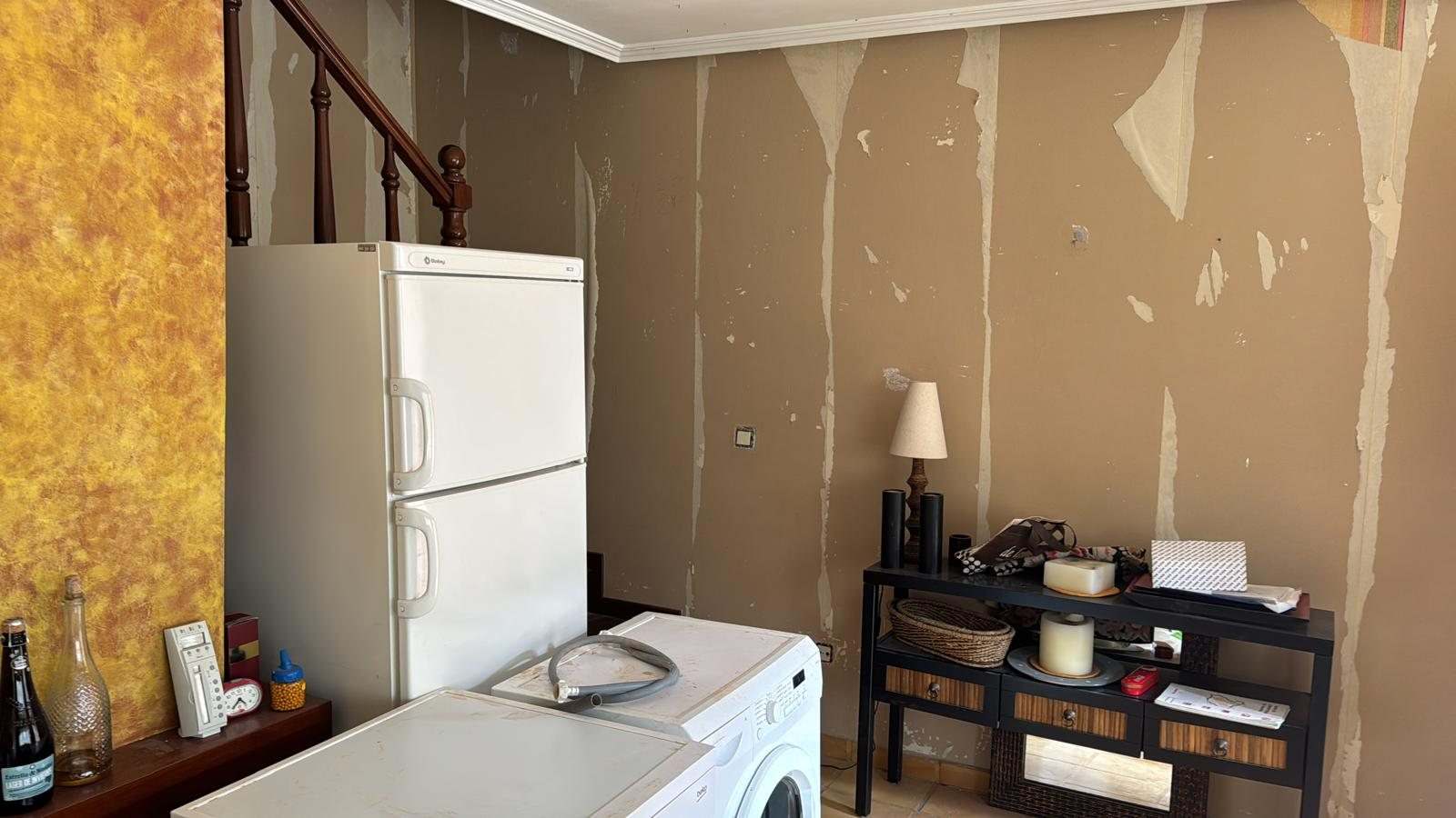 Pared con el papel pintado arrancado y restos de cola, con el frigorífico todavía en su sitio