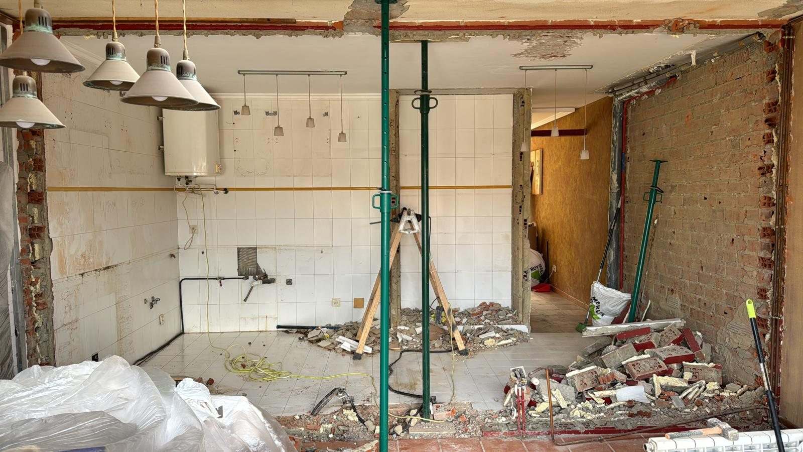 Cocina con el tabique demolido, puntales metálicos sujetando el hueco y escombro en el suelo