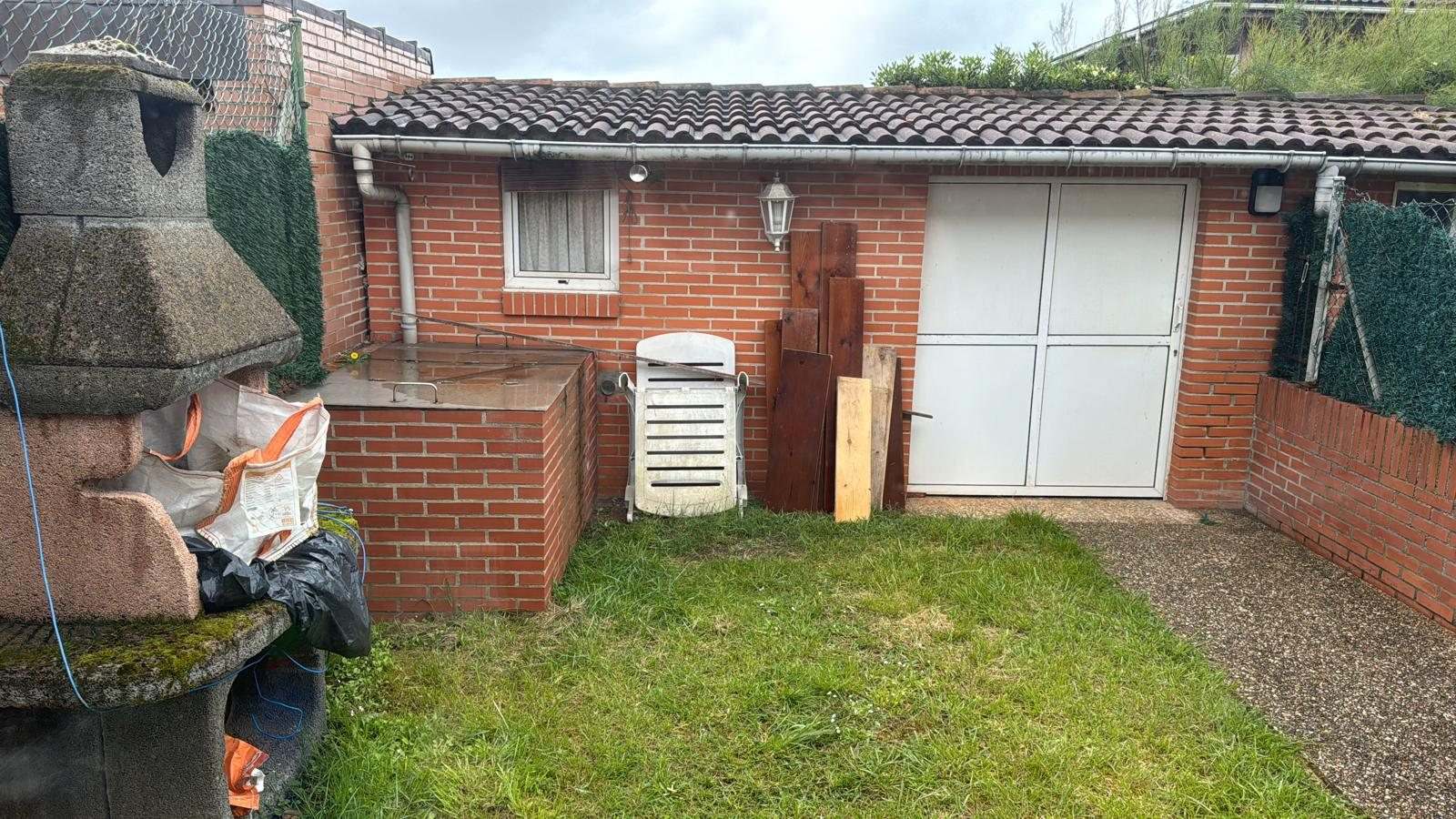 Jardín trasero con césped, barbacoa de obra y caseta de ladrillo con puerta blanca