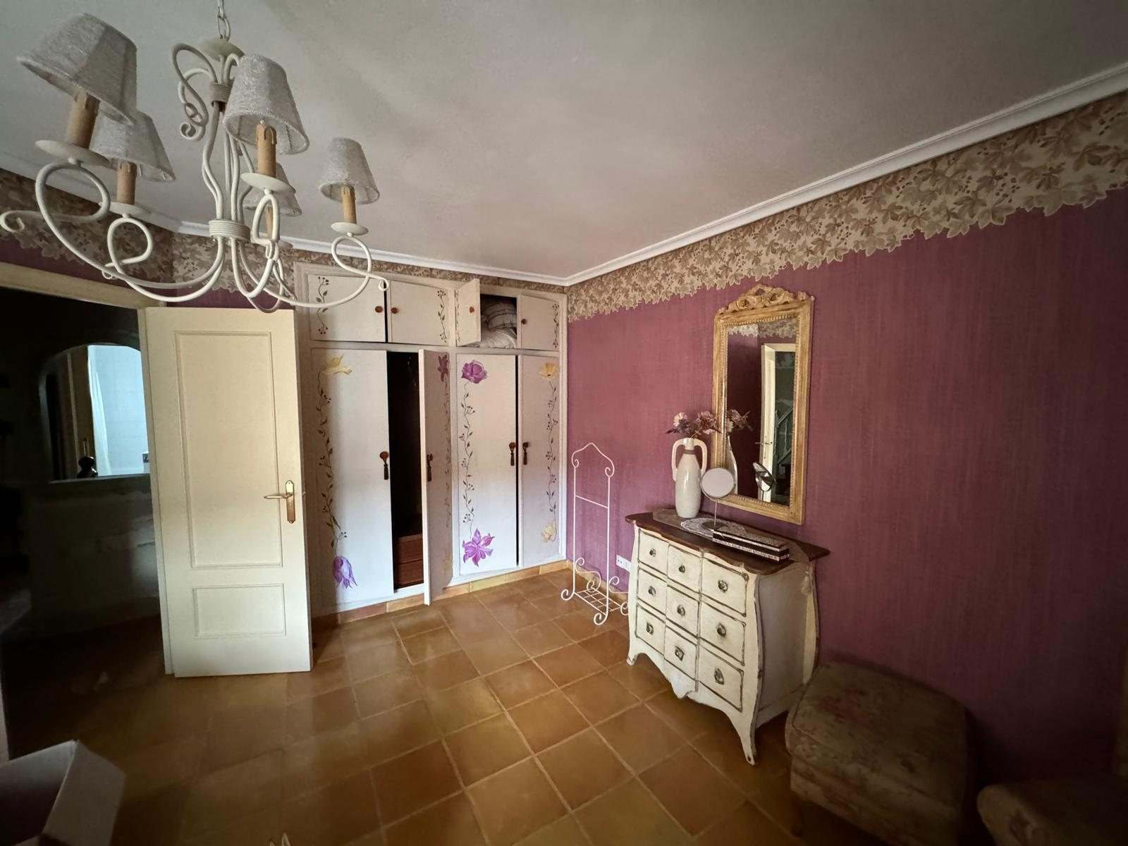 Dormitorio principal con armarios empotrados pintados con flores, cómoda y espejo