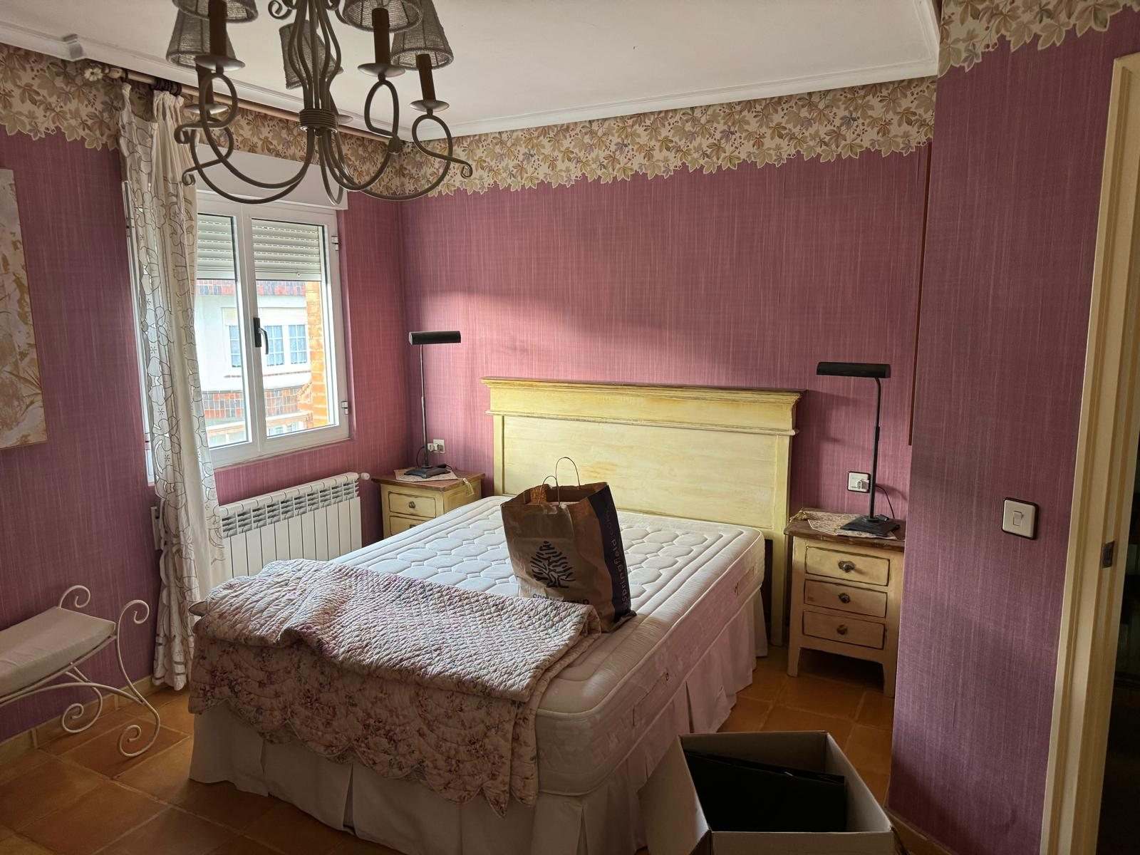 Dormitorio principal con cabecero de madera, ventana y papel pintado granate