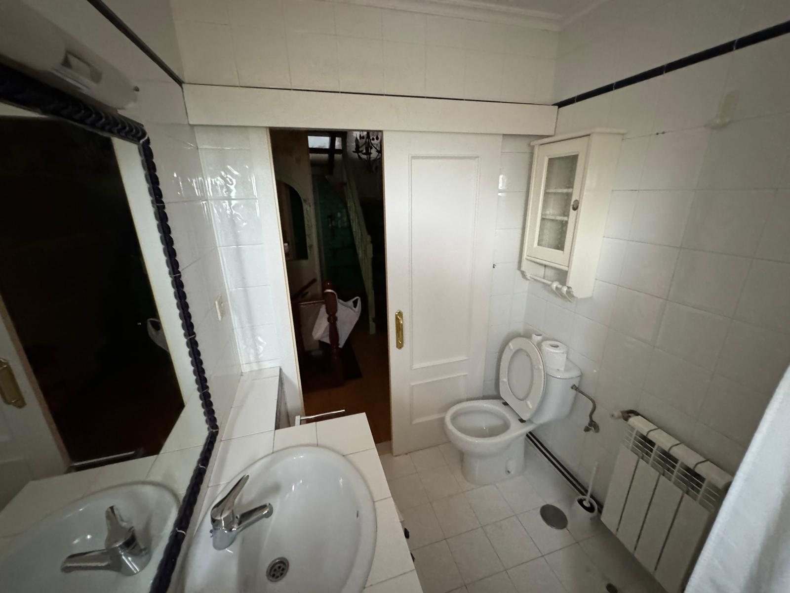 Aseo alicatado en blanco con lavabo, inodoro y puerta corredera