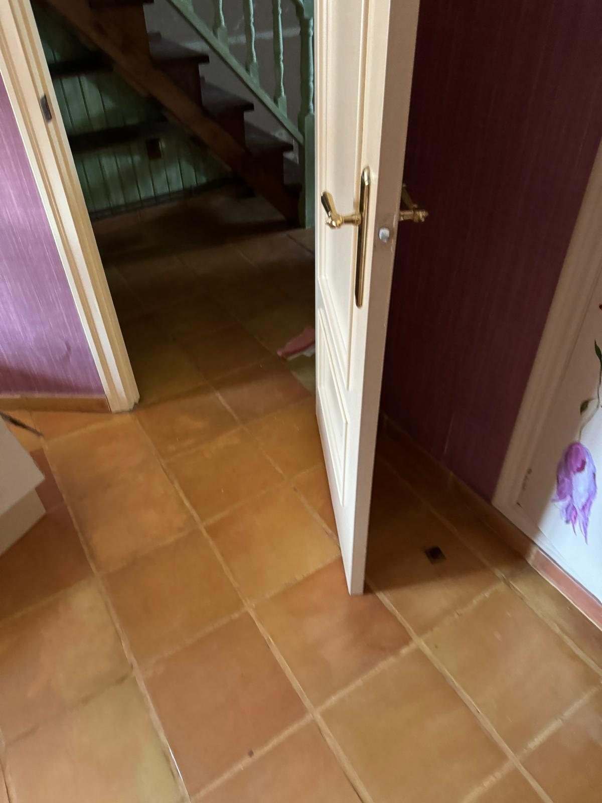 Pasillo con suelo de baldosa de barro, papel pintado granate y la escalera al fondo
