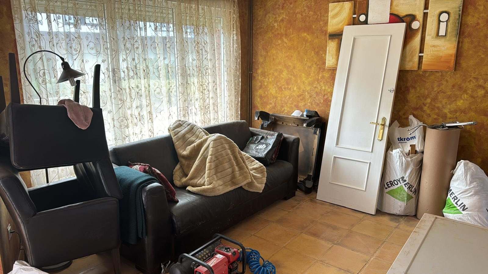 Salón con muebles recogidos, una puerta nueva apoyada en la pared y sacos de material