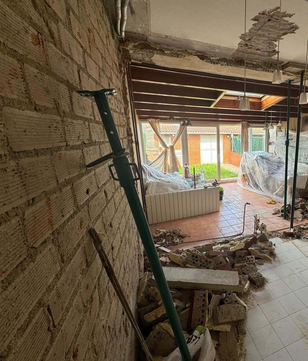 Hueco abierto entre la cocina y el porche acristalado, con un puntal y escombro en el suelo