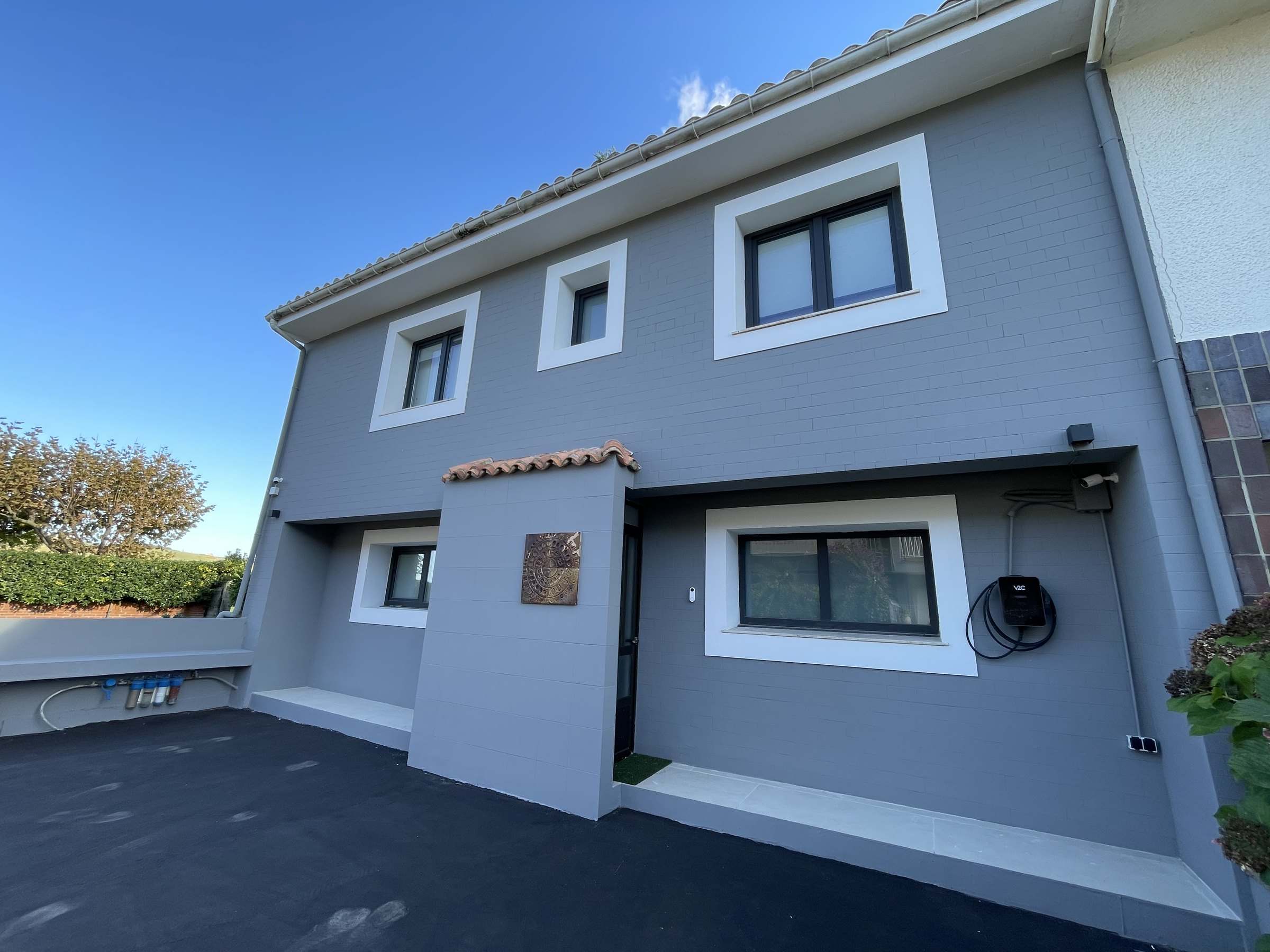 Fachada principal terminada en gris, con recercados blancos en todas las ventanas y el porche de entrada pintado