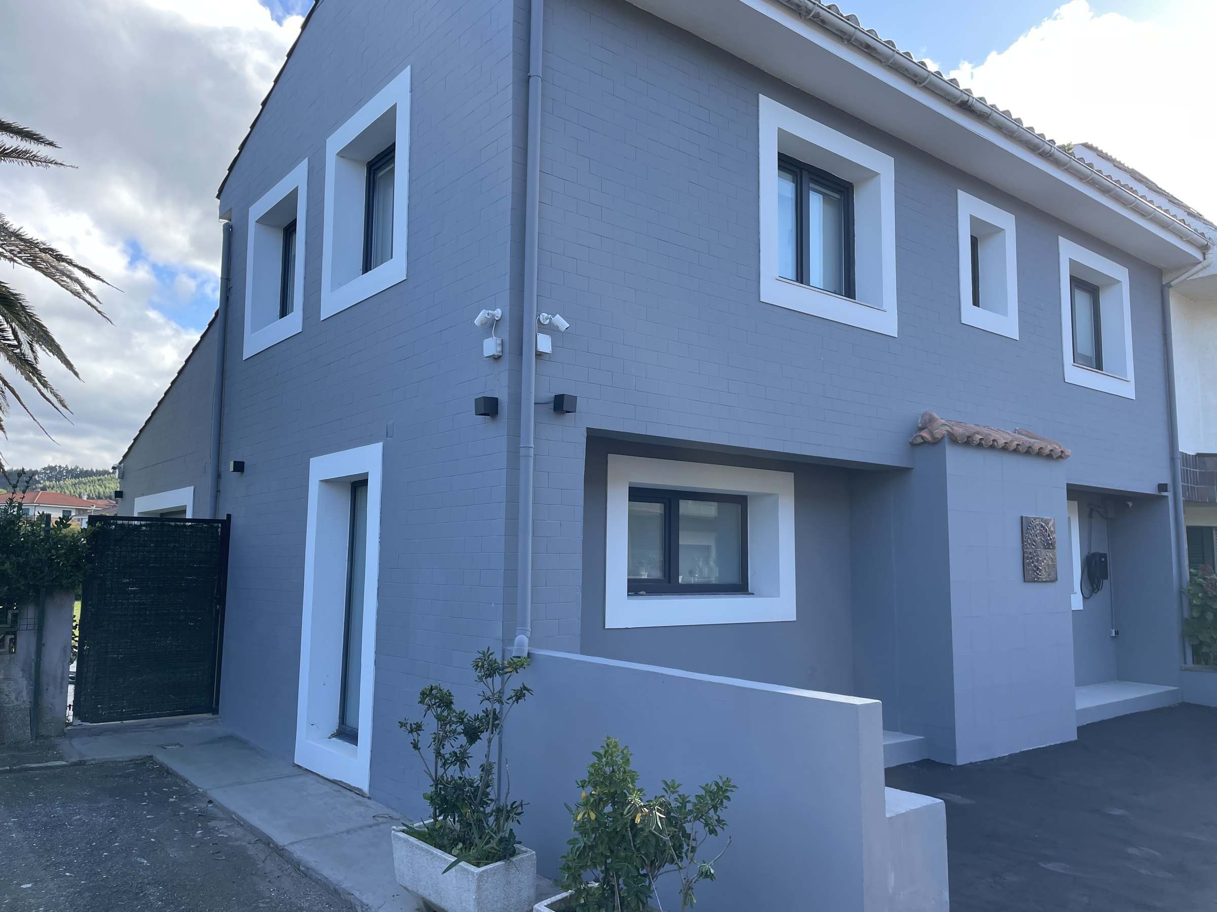 Esquina de la vivienda terminada: fachada lateral y principal en gris con recercados blancos