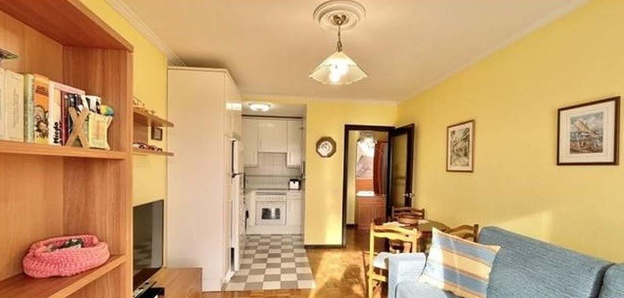 Salón antes de la reforma: paredes amarillas, estantería de madera y, al fondo, la cocina cerrada con suelo ajedrezado