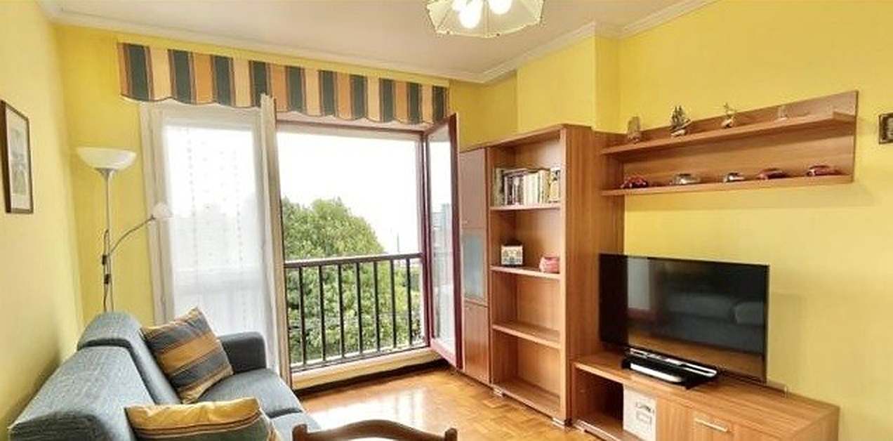 Salón antes de la reforma: sofá azul, mueble de televisión de madera y ventana con toldo de rayas