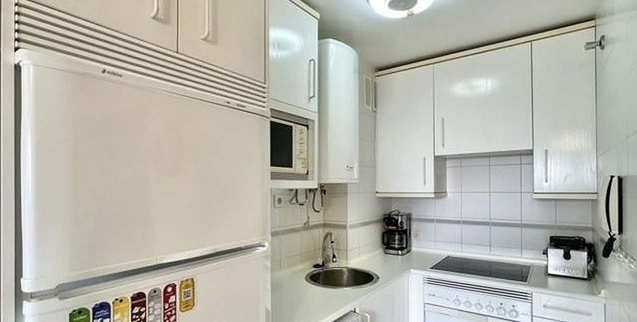 Cocina antes de la reforma: muebles blancos, frigorífico, calentador y alicatado blanco