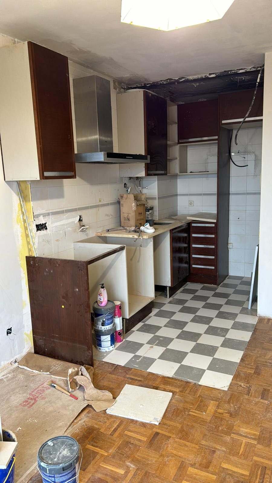 Cocina a medio desmontar: muebles altos oscuros, bajos sin puertas y parte del suelo ajedrezado levantado