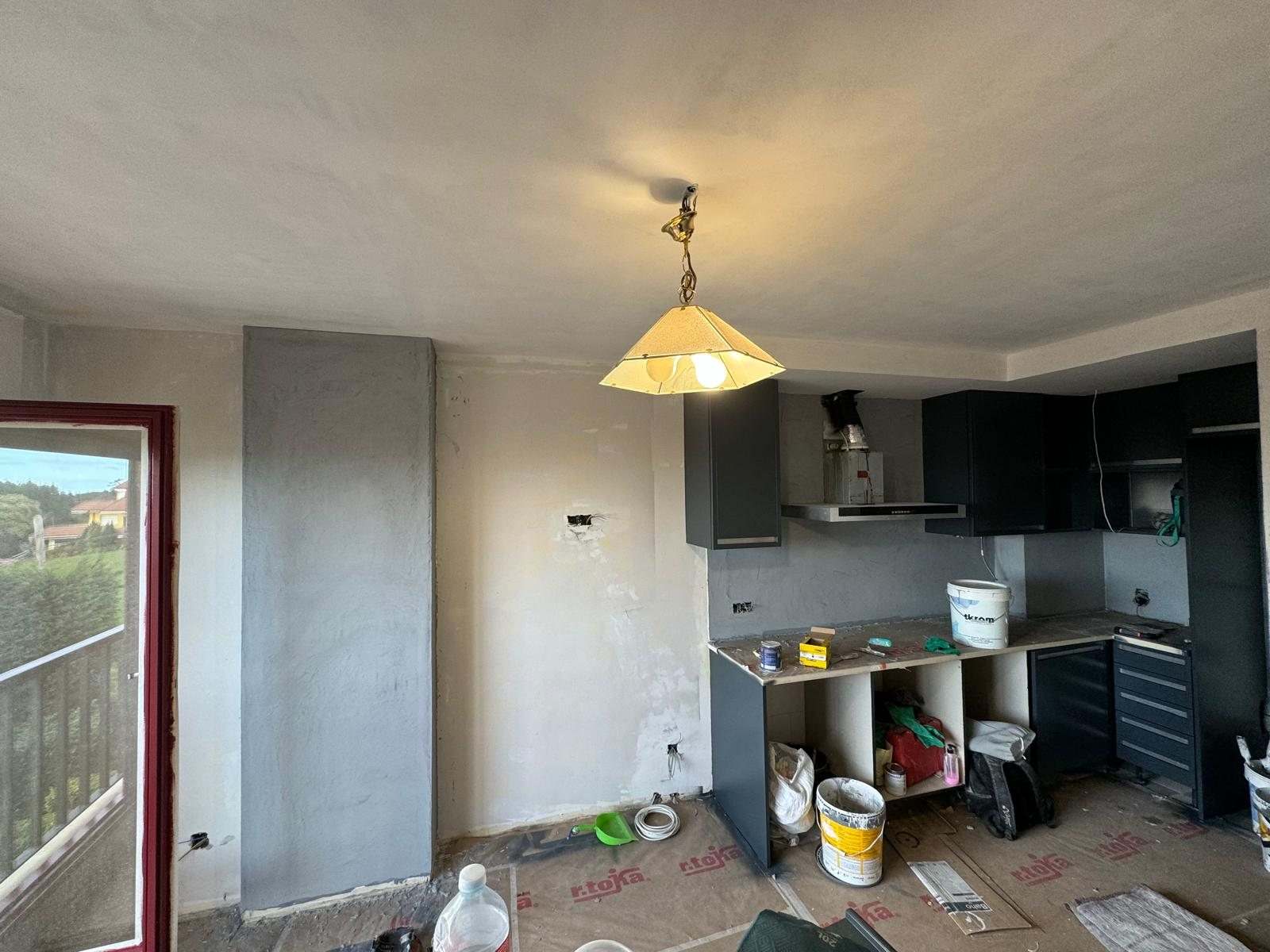 Salón y cocina ya unidos en obra, con el pilar revestido en gris y el suelo protegido