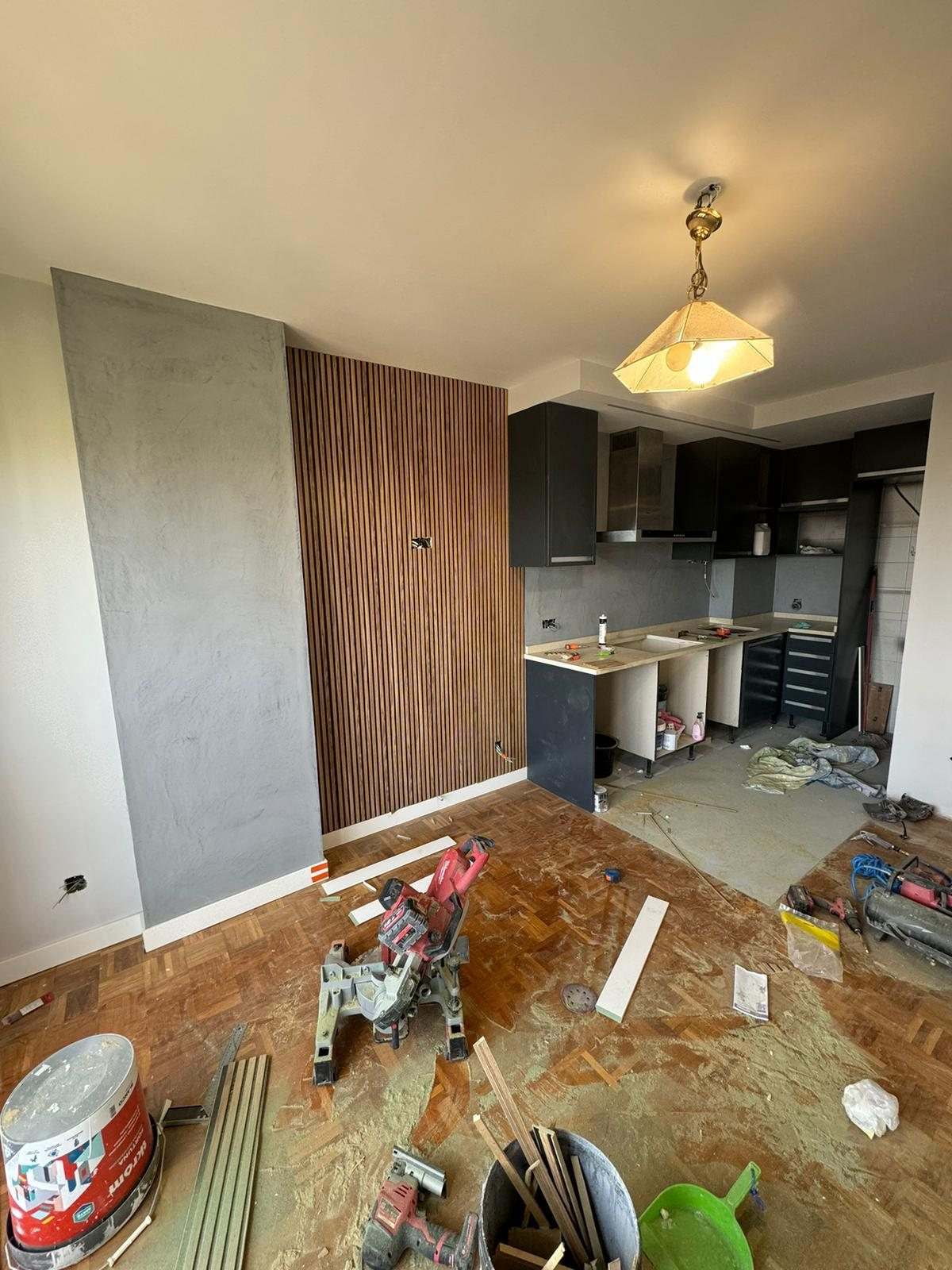 Panel de listones de madera montado junto al pilar gris y muebles de cocina en antracita, con herramientas en el suelo