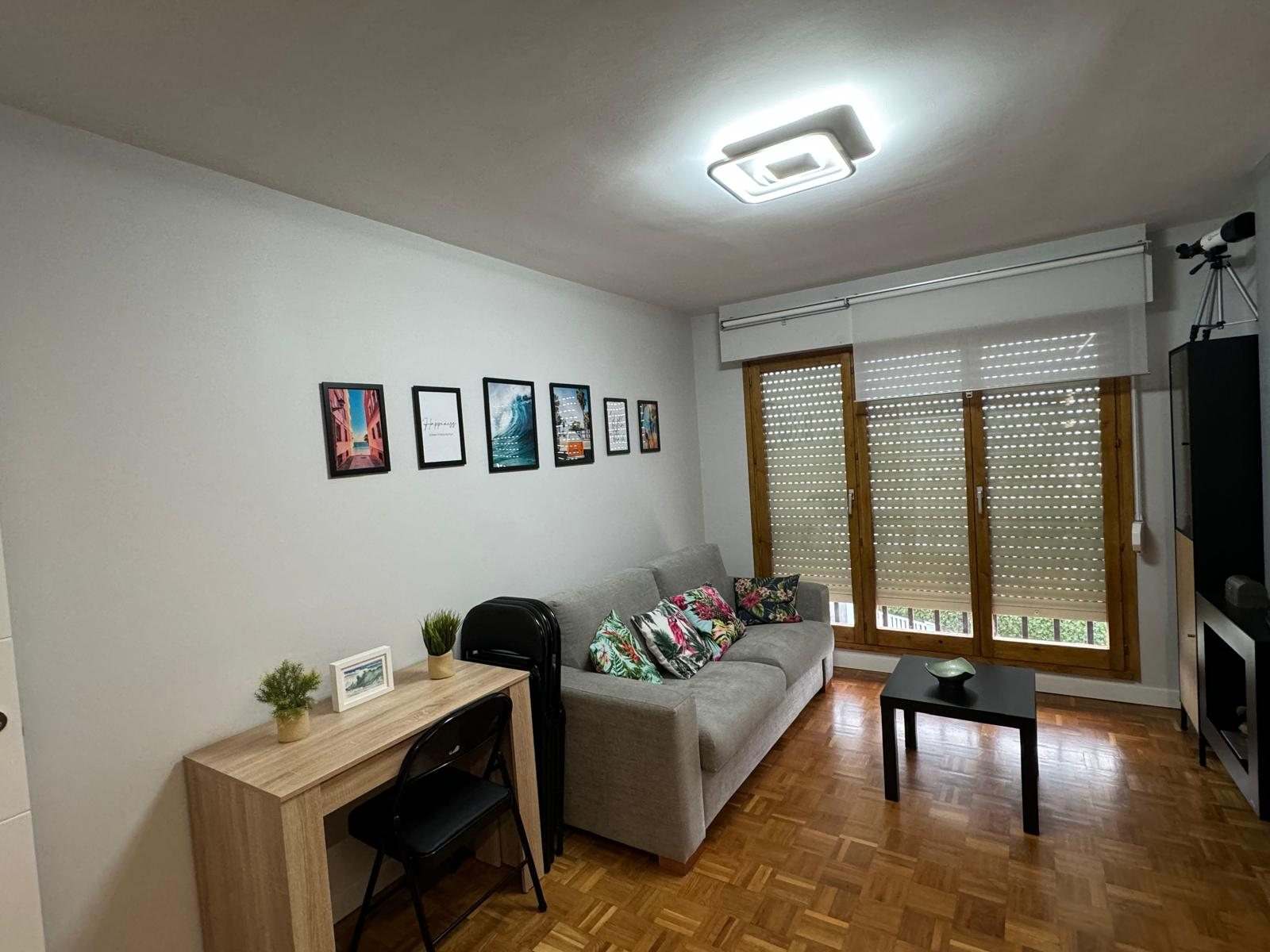 Salón con sofá gris, escritorio de madera clara, cuadros y estores