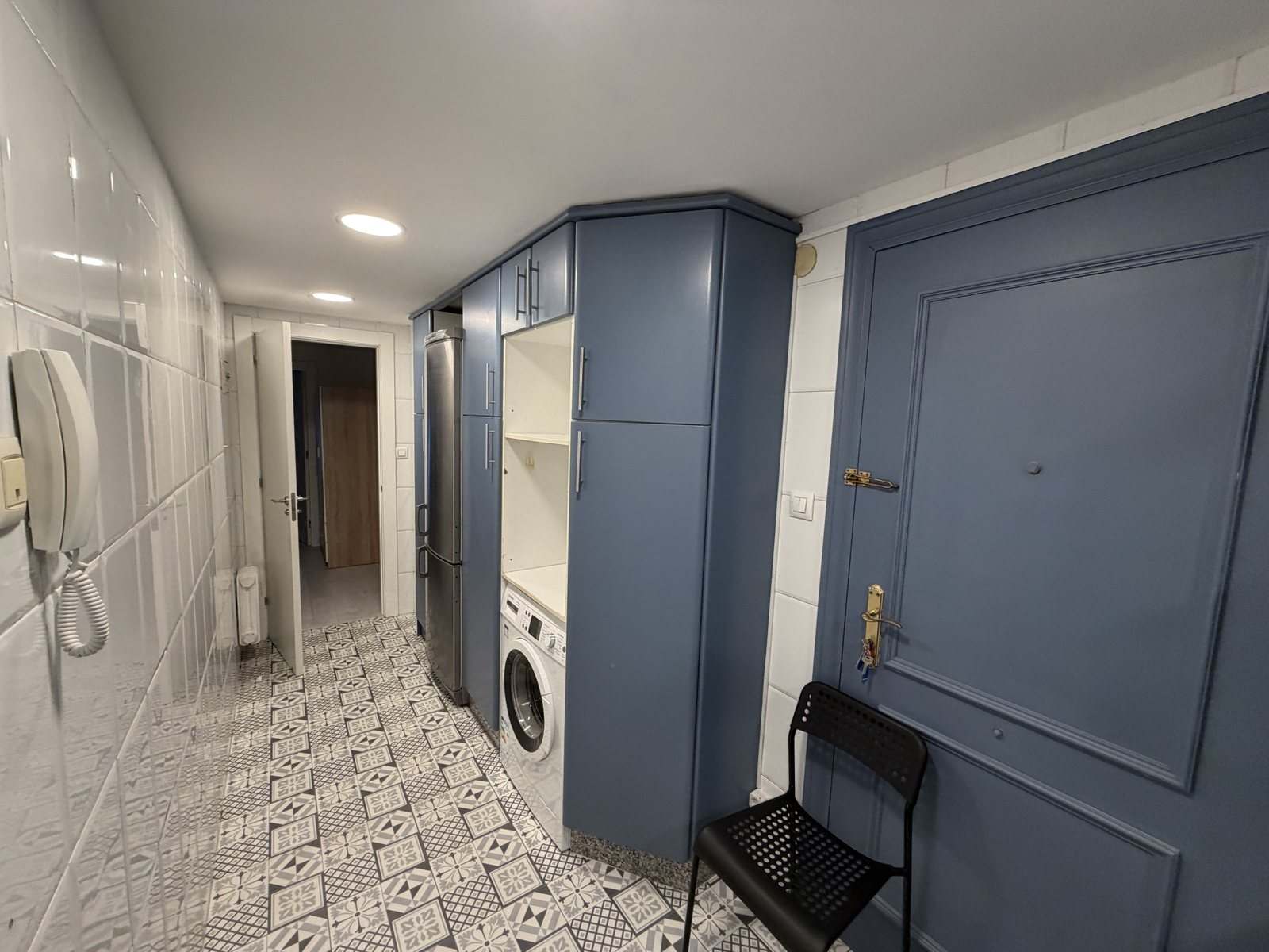 Cocina alargada hacia la puerta, con columna de lavadora y alicatado blanco