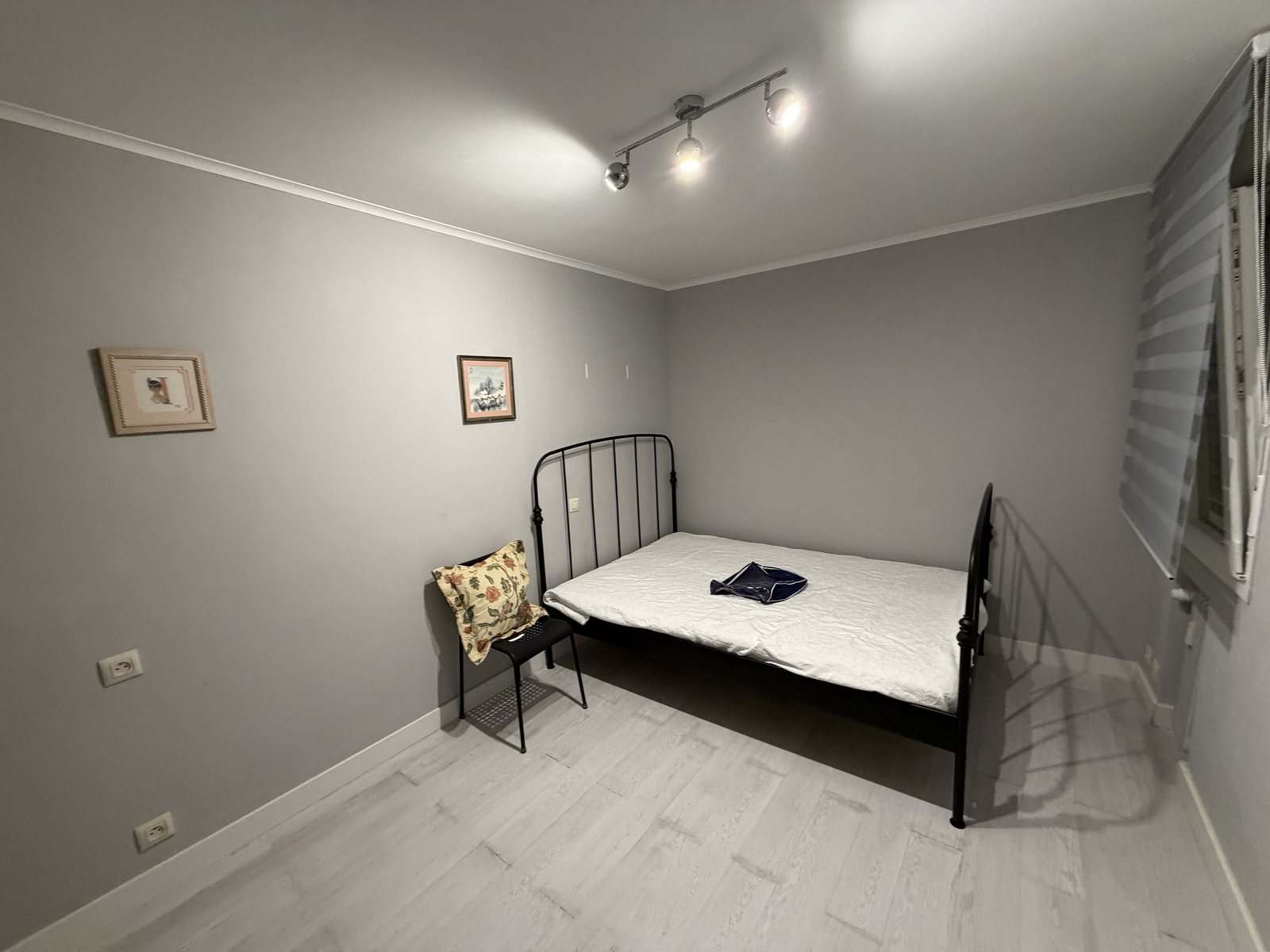 Dormitorio gris con cama de forja negra y estor