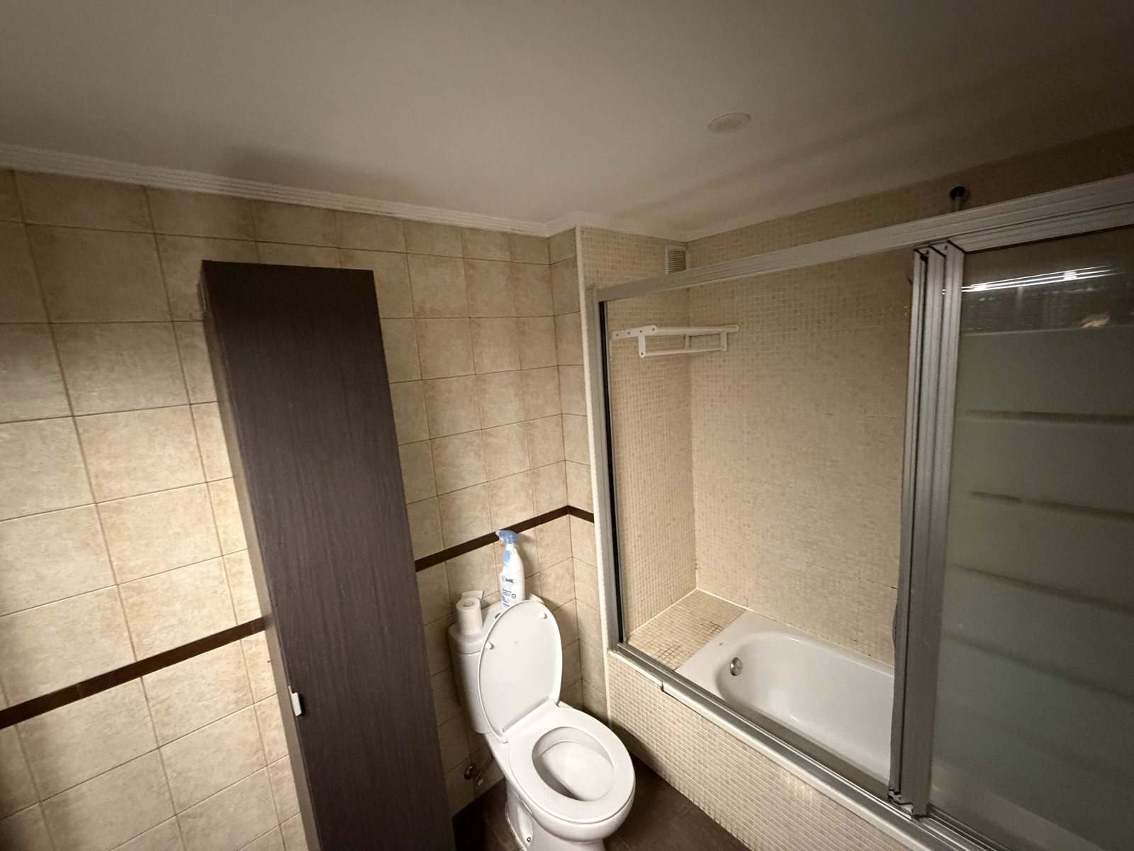 Baño alicatado en beige con bañera, inodoro y mueble columna