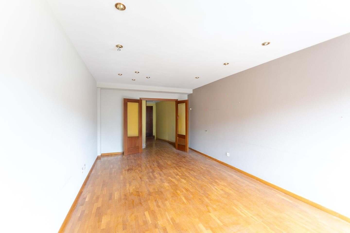 Salón visto hacia la puerta del pasillo, con suelo de parquet y focos empotrados en el techo