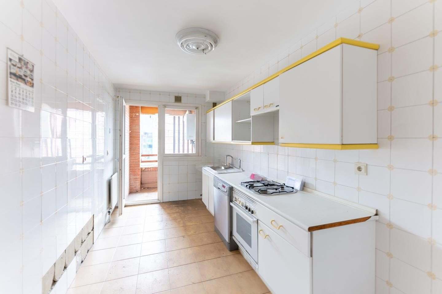 Cocina alargada con muebles blancos de cantos amarillos, alicatado blanco y puerta a la terraza