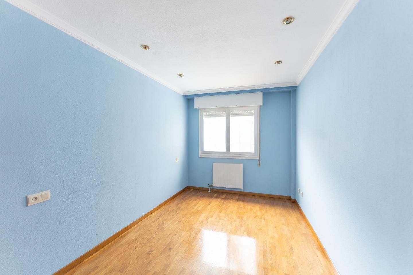 Dormitorio con paredes azules, suelo de parquet y ventana