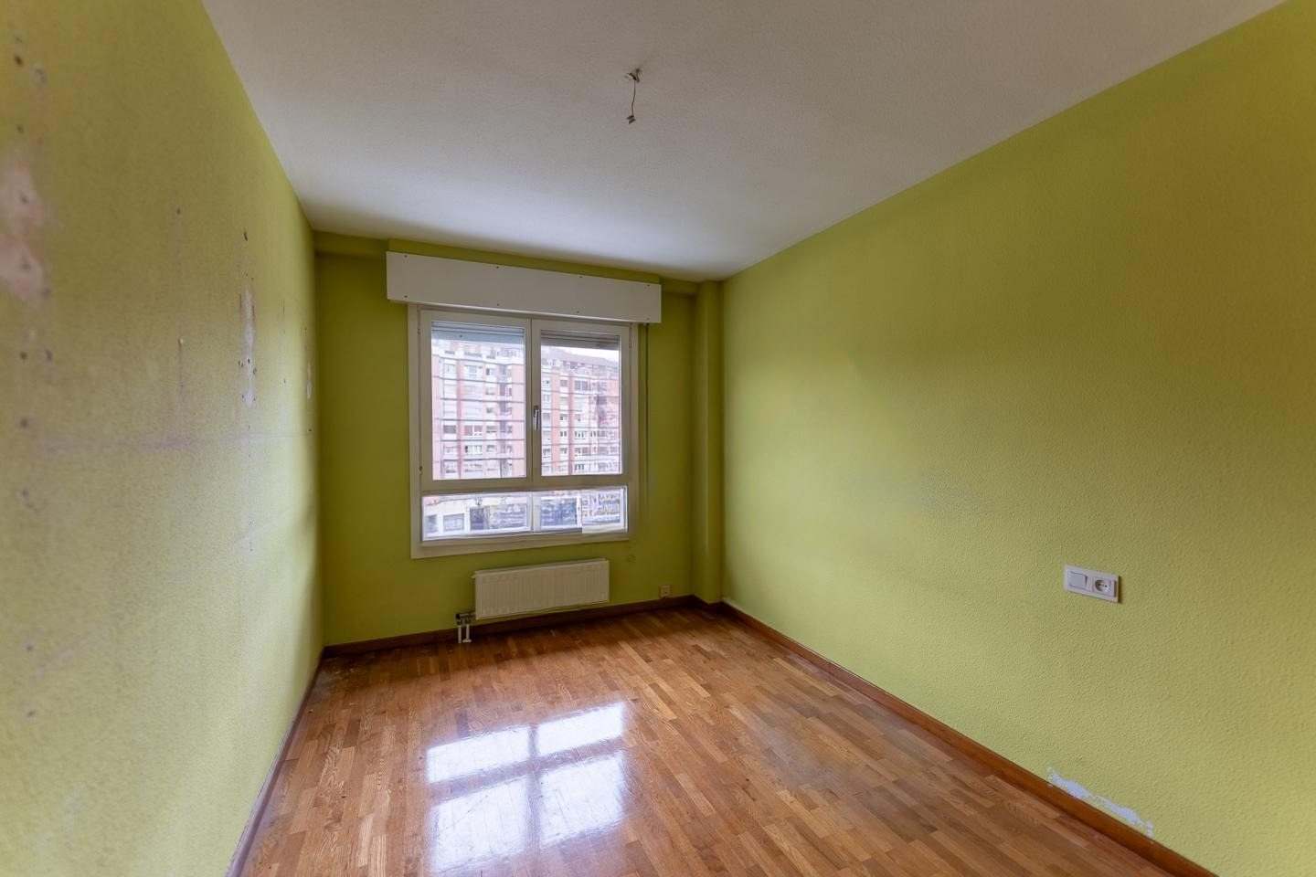 Dormitorio con paredes verdes, suelo de parquet y ventana a la calle