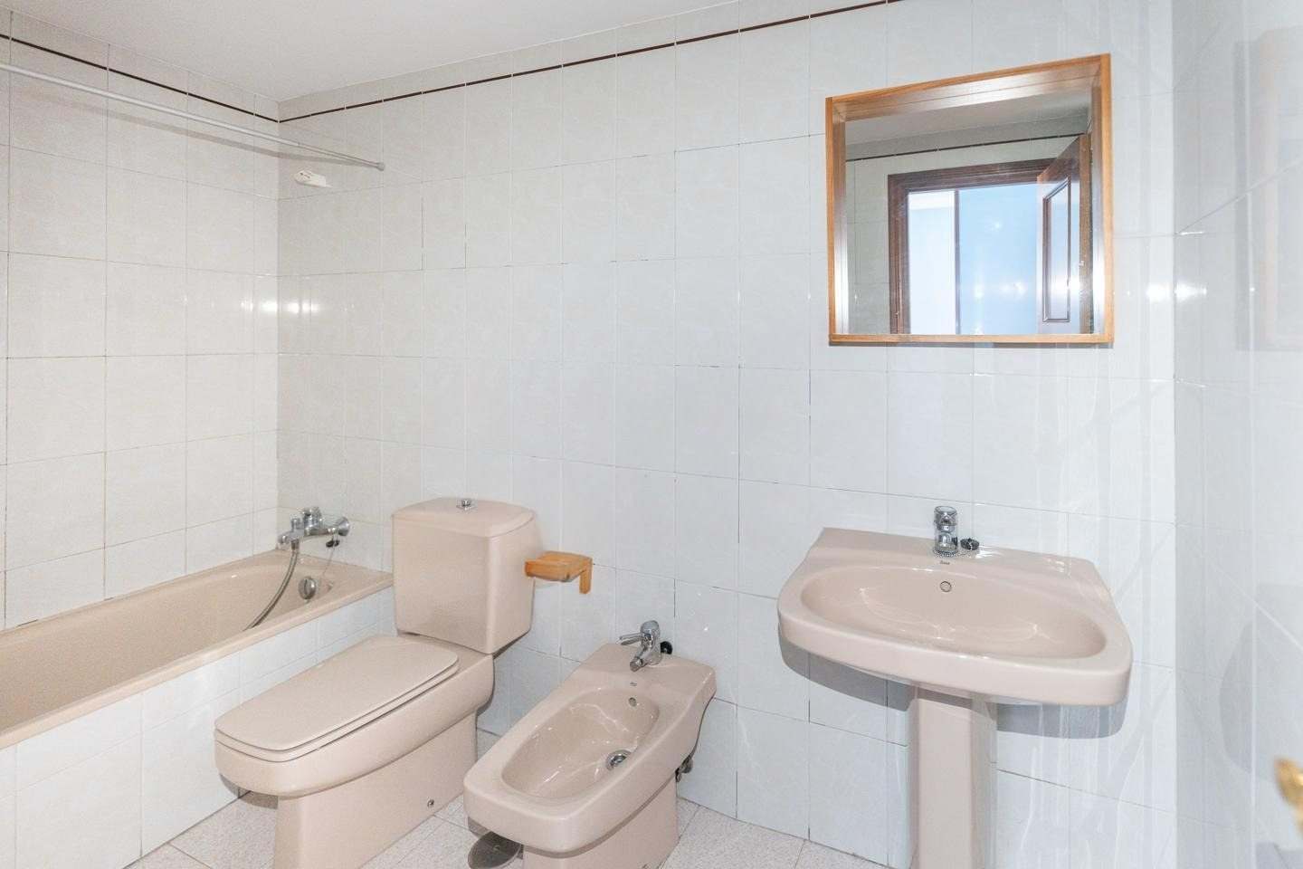 Baño con bañera, inodoro, bidé y lavabo en color rosa y alicatado blanco